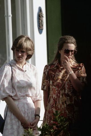 Princess Diana wearing a pink dress standing next to Princess Anne in 1981 wearing sunglasses and an orange printed dress