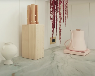 Sarah Paulson's marble kitchen countertop with a ceramic pot, wooden knife block, and pastel pink gooseneck kettle