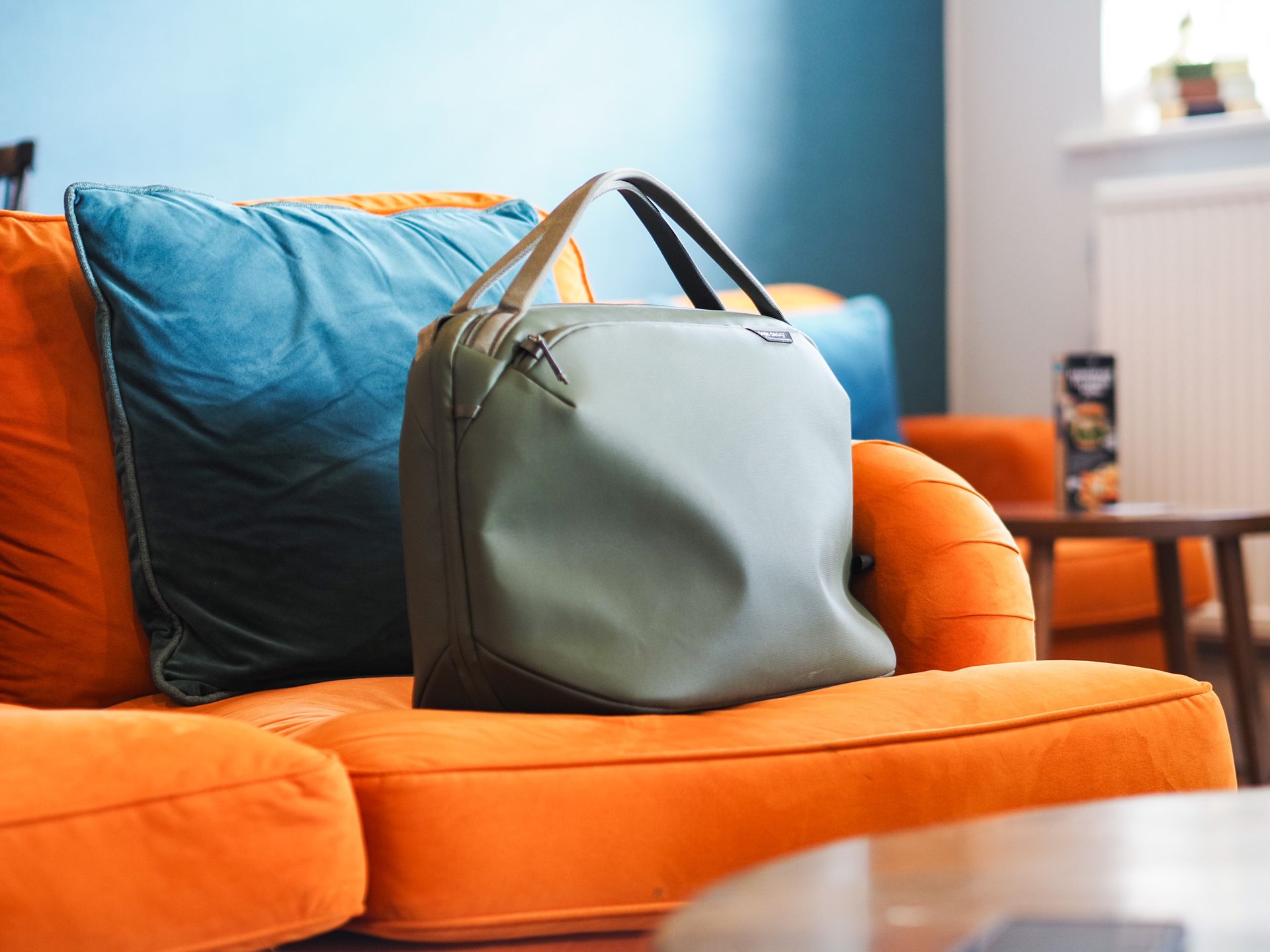 The Peak Design Travel Weekender 25L in sage green, on a bright orange sofa