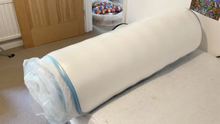 The Linenspa Memory Foam Hybrid Mattress rolled up in plastic on a bed frame