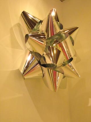 Metallic gift wrapping bow photographed on a yellow surface