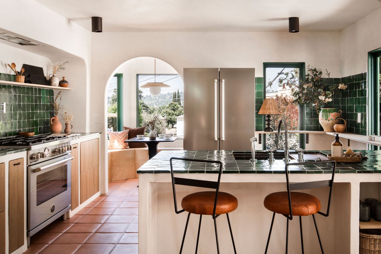 A kitchen with green tiles on counter and backsplash, red-toned flooring and a counter with seating