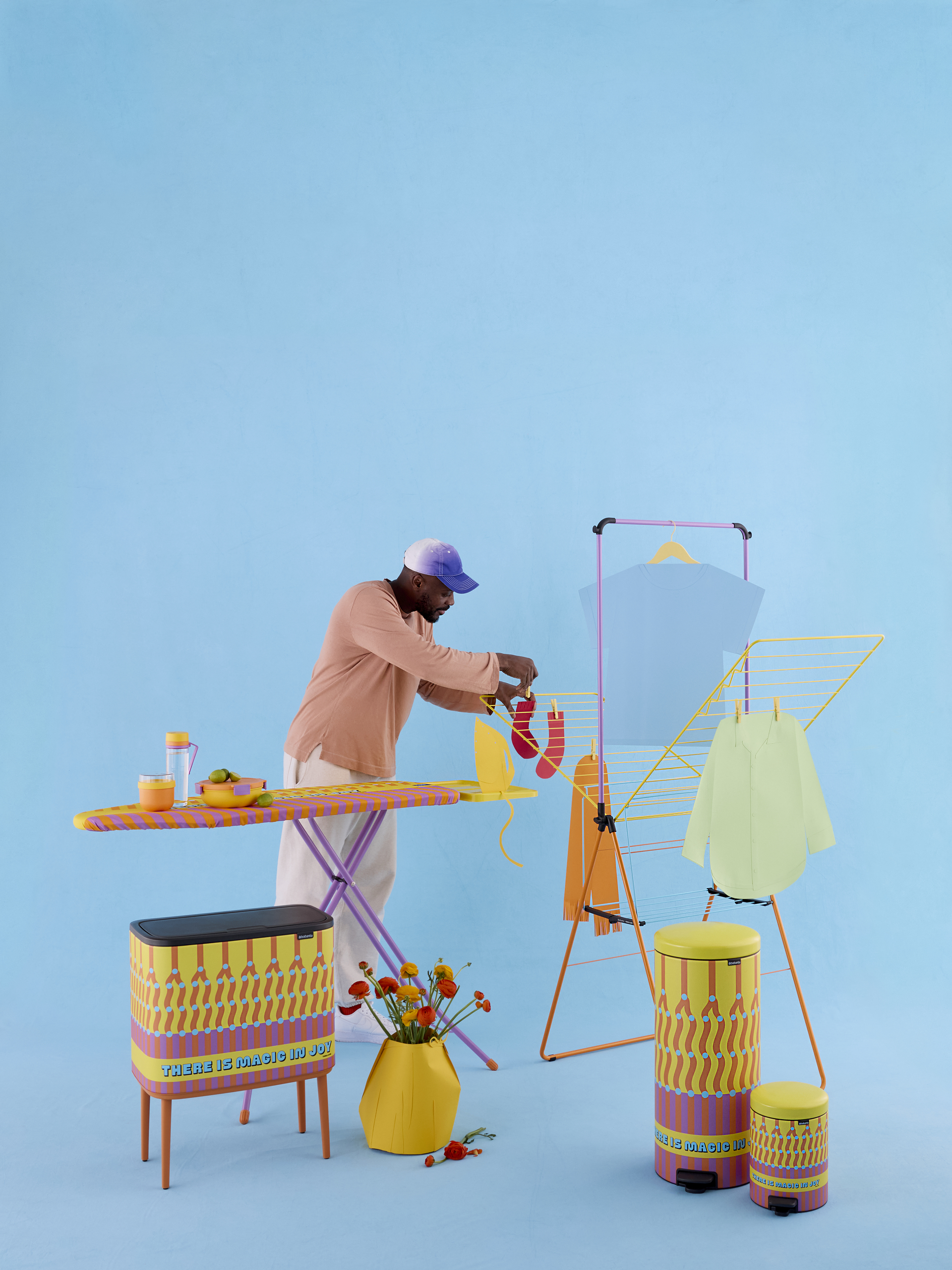 Image of a person standing in a bright blue showroom surrounded by practical, colorful homeware products like trash cans and drying racks. He's hanging a sock on the drying rack.
