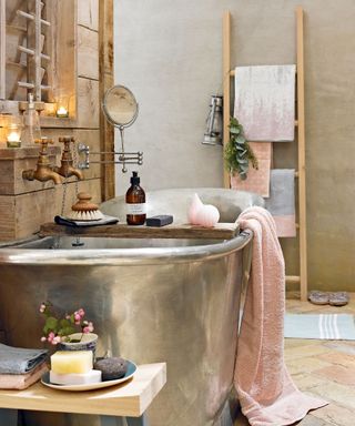 Luxurious natural style bathroom with polished tin bath, pastel coloured towels and luxurious unguents.
