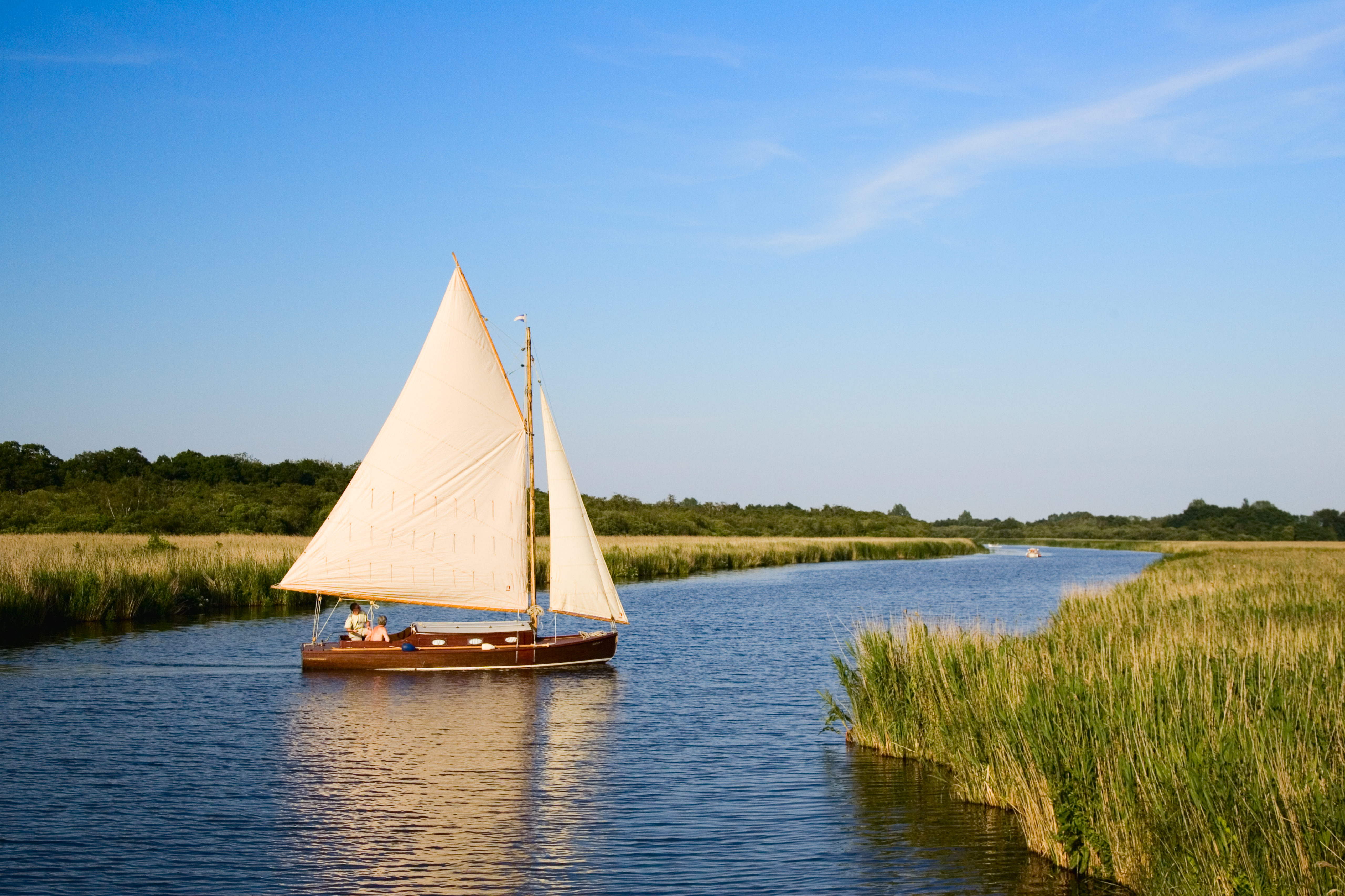 Single small sailboat with a brown wood hull and cream sails on the Norfolk Broads
