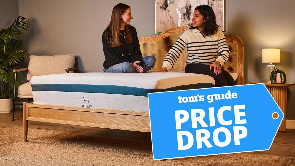 Two women sit on the Helix Twilight Mattress on a bed frame in a comfortable bedroom, a Tom&#039;s Guide price drop deals graphic (left)