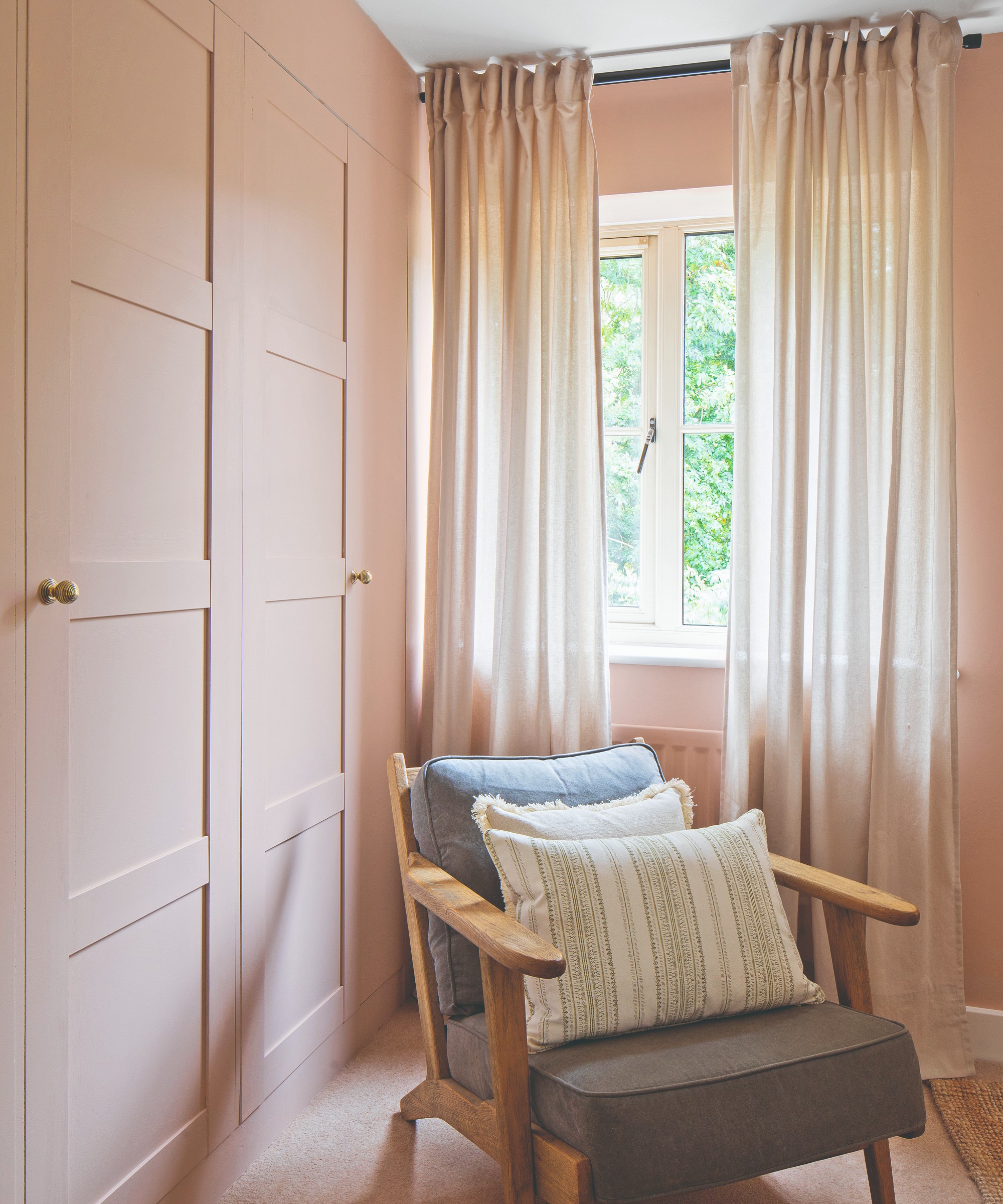 A pink-painted bedroom with tonal voile curtains on the windows