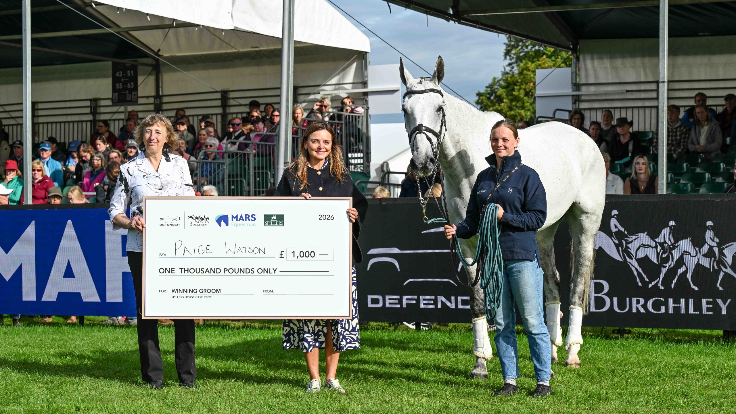Paige Watson stands with Deerpairc Revelry beside a giant cheque for &pound;1,000, presented by two women, at Burghley Horse Trials