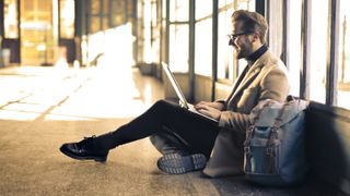 Man using a laptop while sitting on the floor next to his backpack