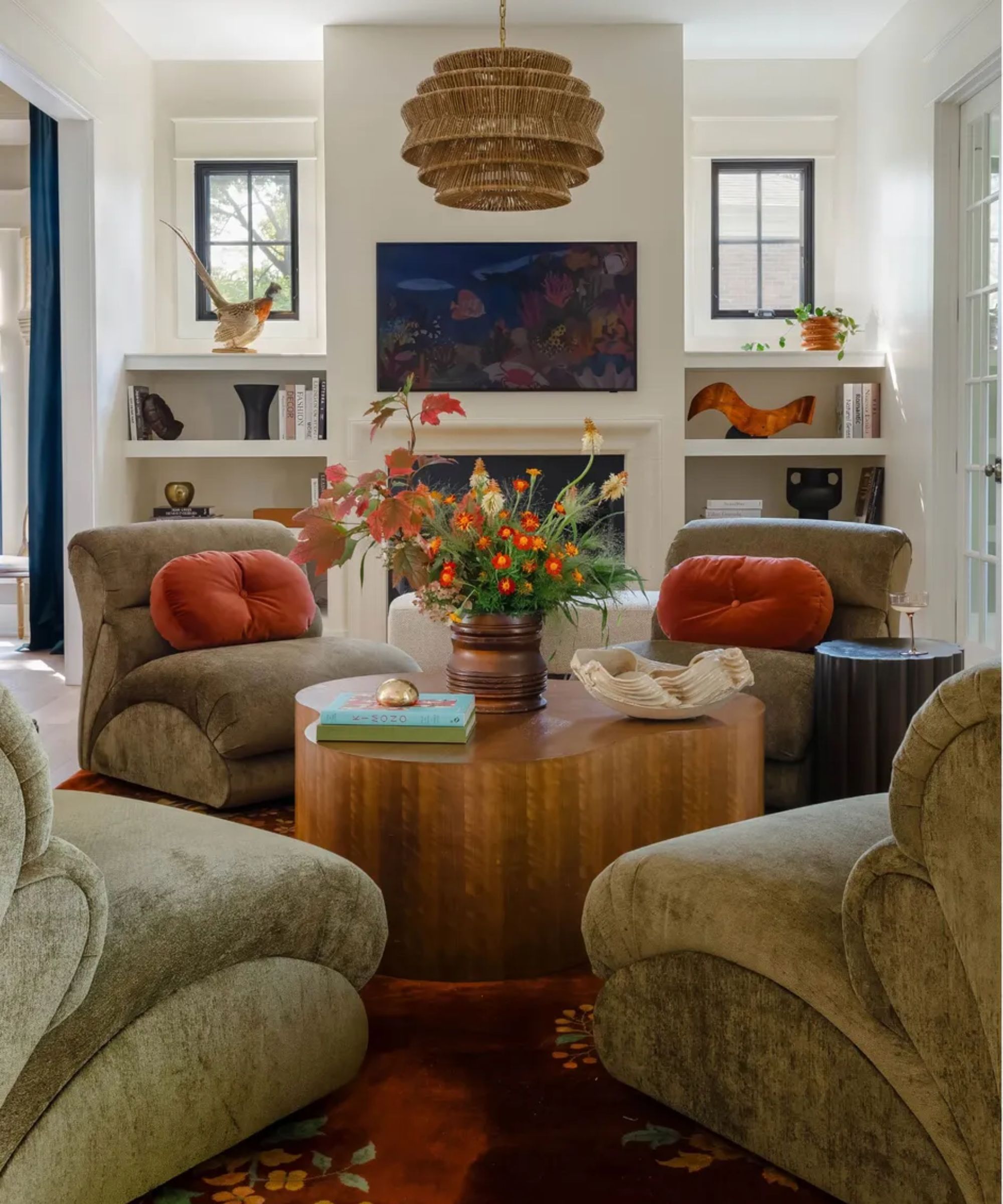 Cozy living room, four chairs around a round wooden coffee table with flowers, fireplace and decorated alcove shelving in background