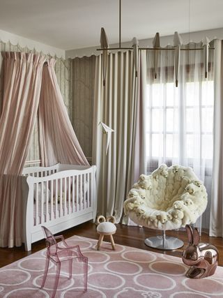 baby girl nursery with pink canopy over cot, pink rug, Cole & Son wallpaper, sculptural pendant, armchair