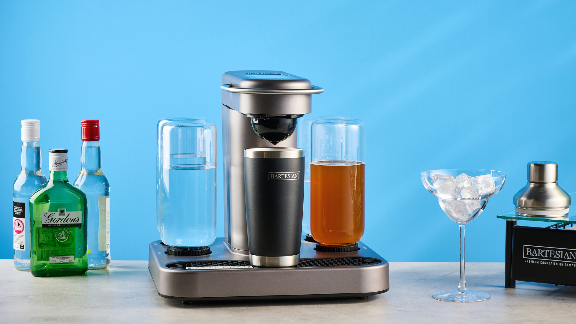 the bartesian premium cocktail machine photographed against a blue background showing its drink-making abilities and accessories and functionality with cocktail pods