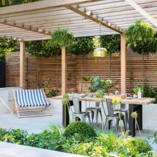 Garden with wooden panelling, pergola, table and deck chair
