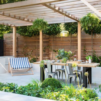 Garden with wooden panelling, pergola, table and deck chair