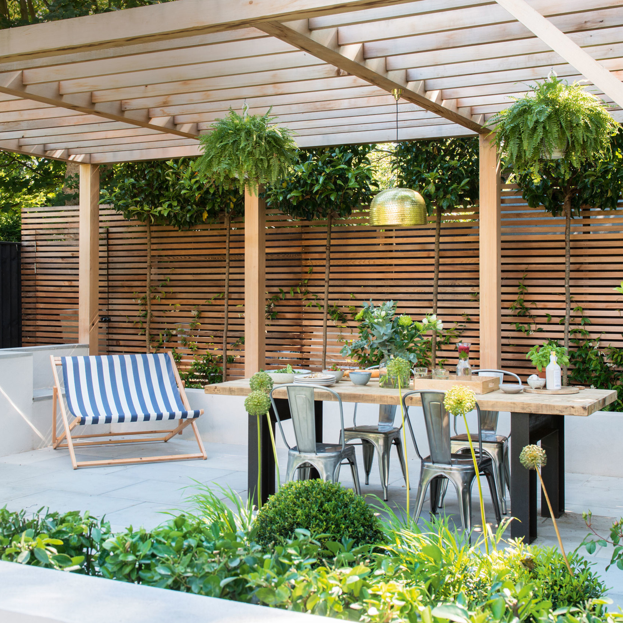 Garden with wooden panelling, pergola, table and deck chair