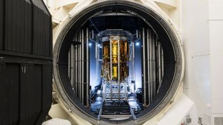 a gold-foiled spacecraft stands in a chamber with an open hatch