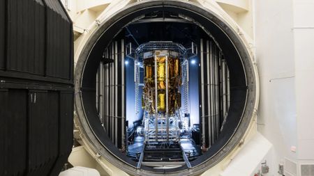 a gold-foiled spacecraft stands in a chamber with an open hatch