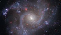 A swirl of purple and blue gas dotted with red stars moves around a central glowing core, blending together to make a giant spiral galaxy.