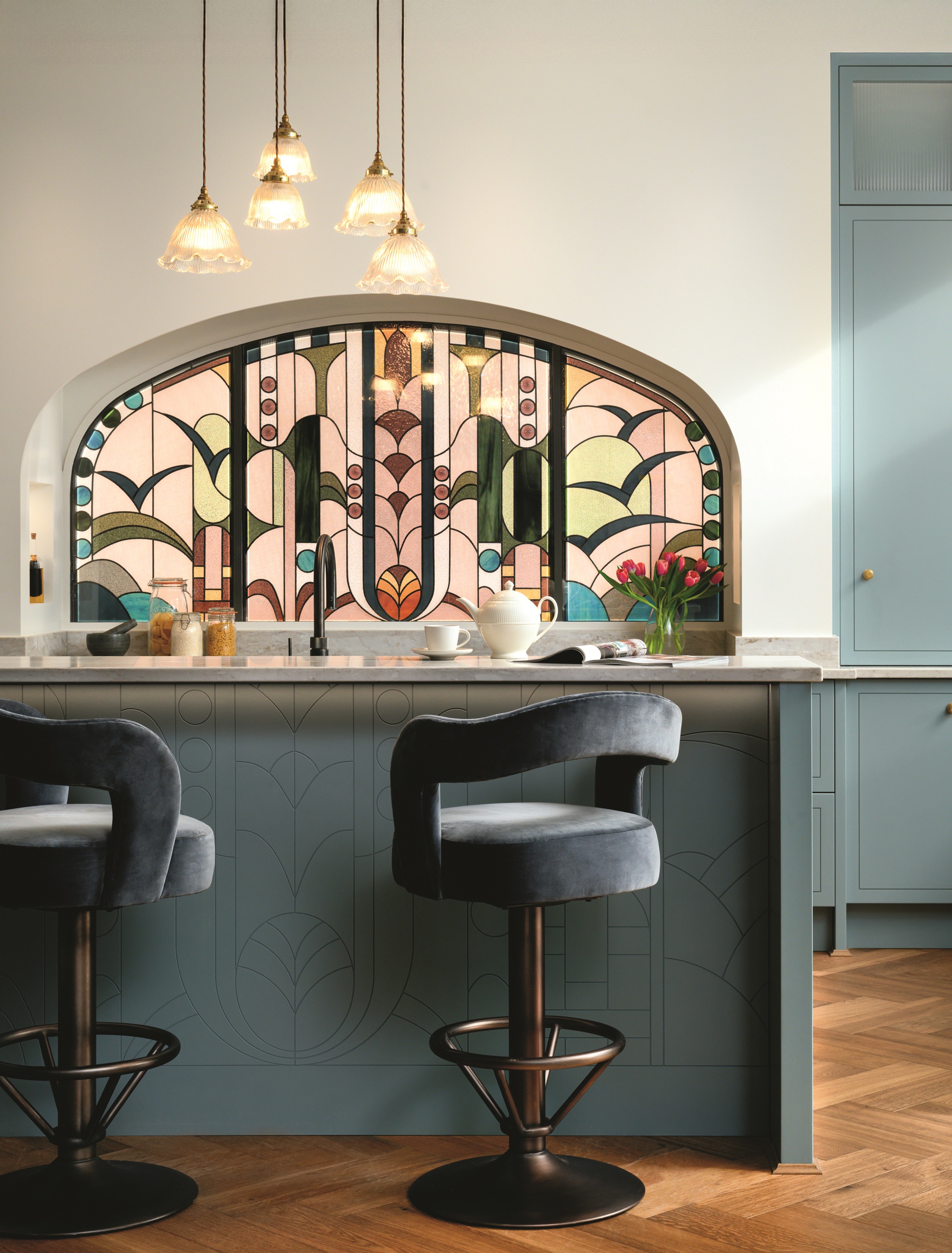 modern kitchen with blue cabinetry, white walls, and stained glass backsplash, with blue swivel bar stools and pendant lights