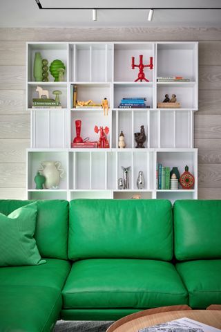 An emerald green couch pops in front of a curated bookshelf of knickknacks.