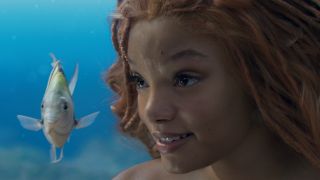 Halle Bailey smiling under the sea, with Flounder next to her in The Little Mermaid.
