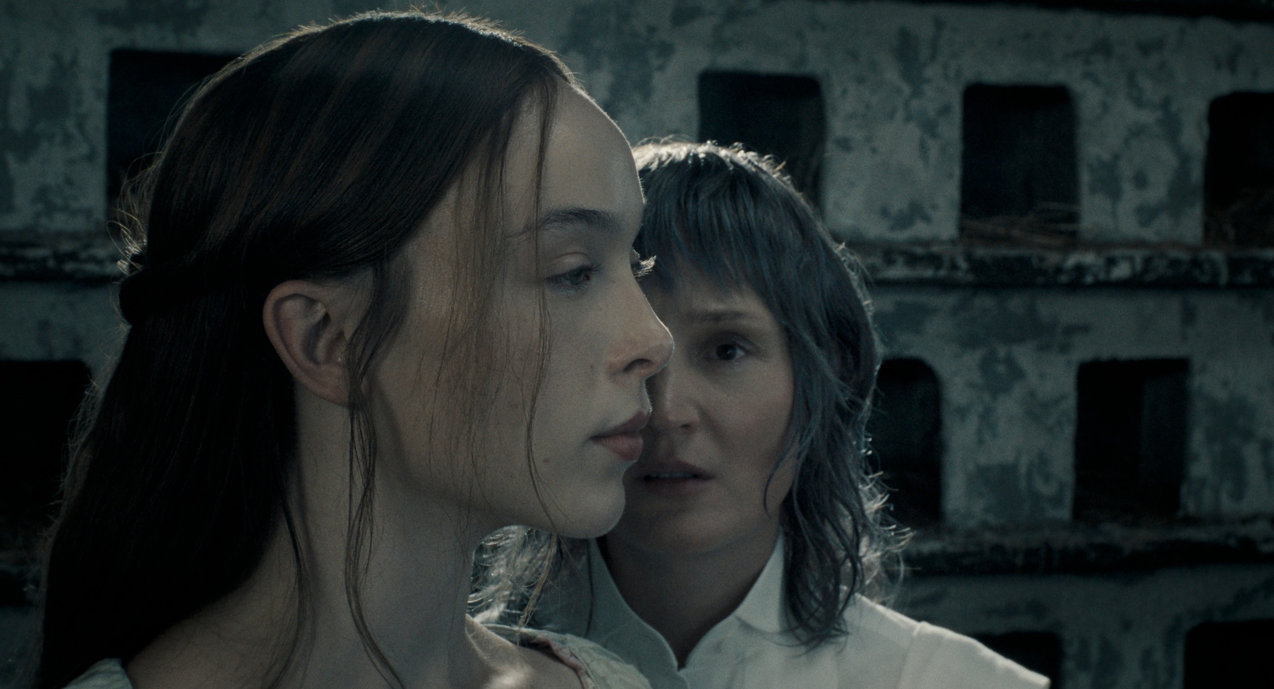 ella beatty as lizzie borden looking ahead while vicky krieps as bridget sullivan stands to the side of her profile in a dimly lit still of the show monster the lizzie borden story