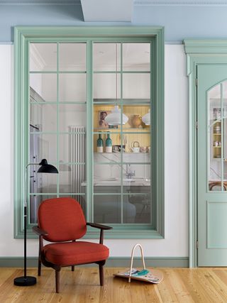 modern kitchen separated from a living room by a white partition wall with green framing