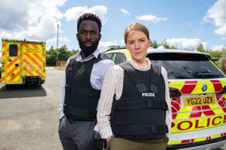 Gemma Whelan as DS Sarah Collins and Jimmy Akingbola as DC Steve Bradshaw standing in front of a police car.