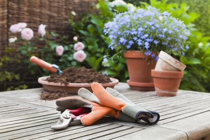 A small outdoor table with a pair of gardening gloves, pots, and a pile of soil