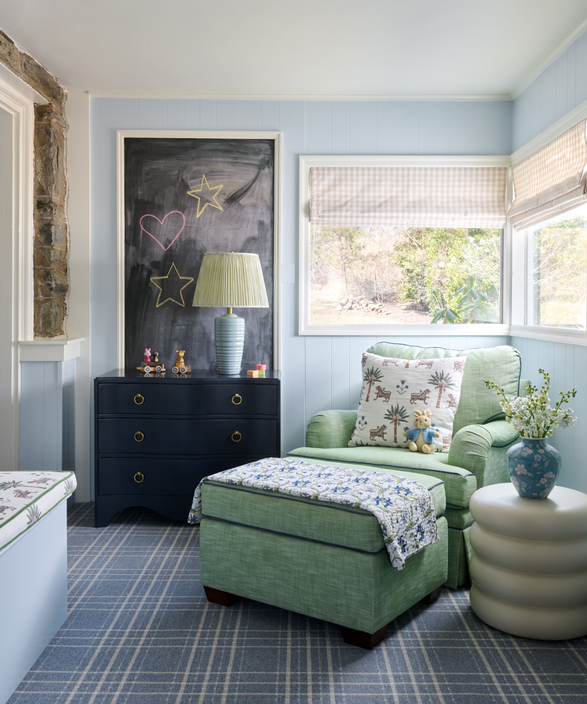 A nursery room with powder blue walls, a dark blue carpet and a large green armchair.