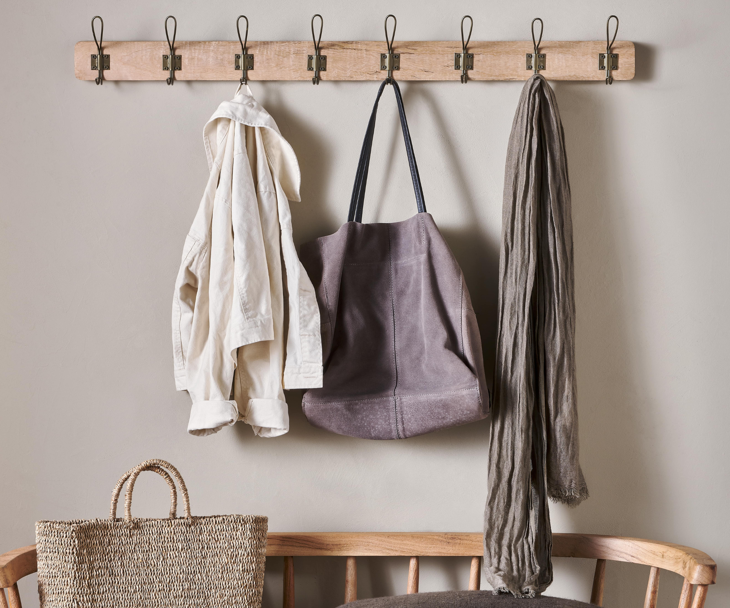 clothing and bags hung up on a wooden wall mounted peg strip with wooden chair beneath