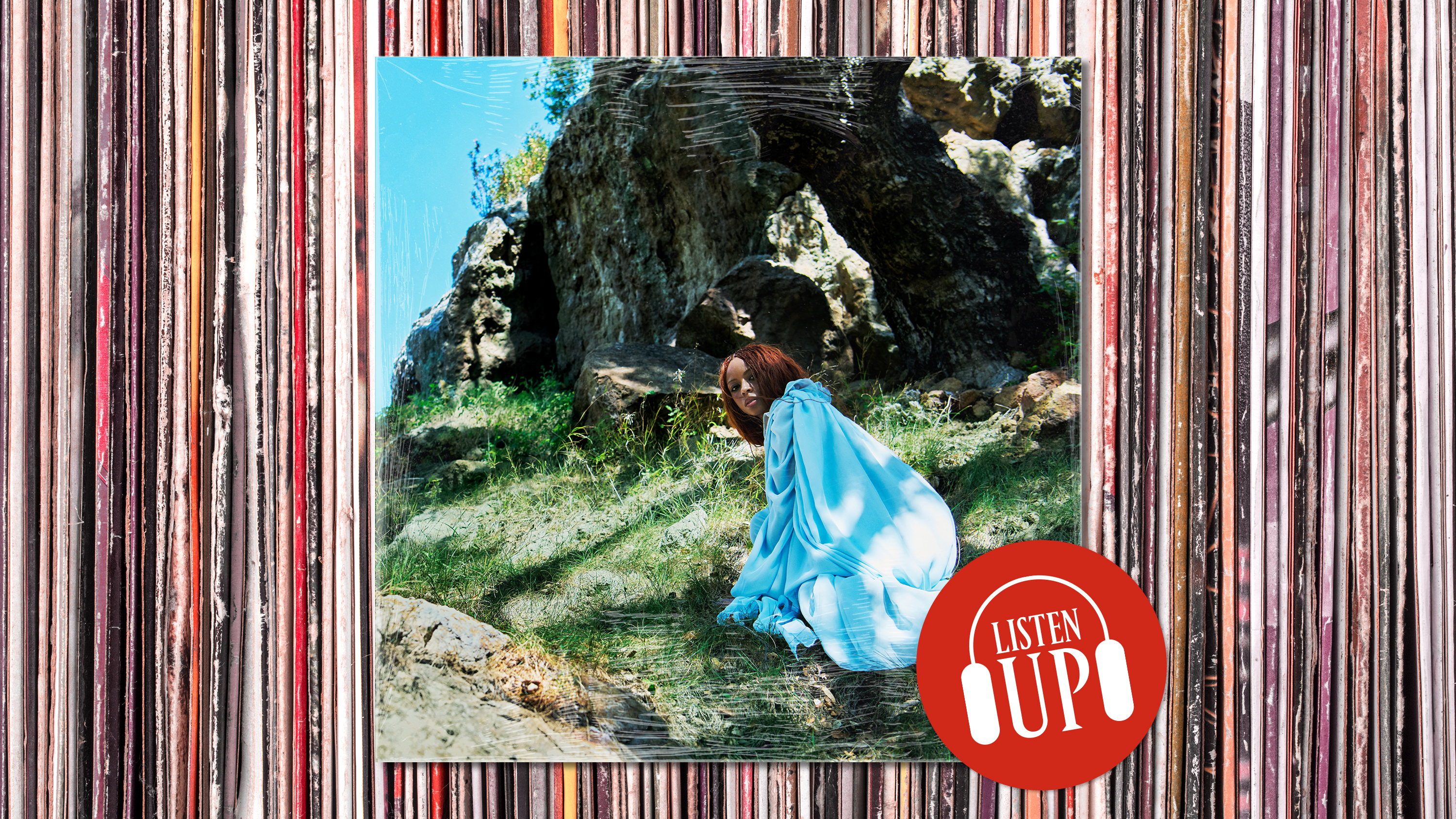 singer ravyn lenae wearing a blue dress looks over her shoulder while climbing up a mountain on the cover of her album blue island designed around the marie claire listen up franchise stamp
