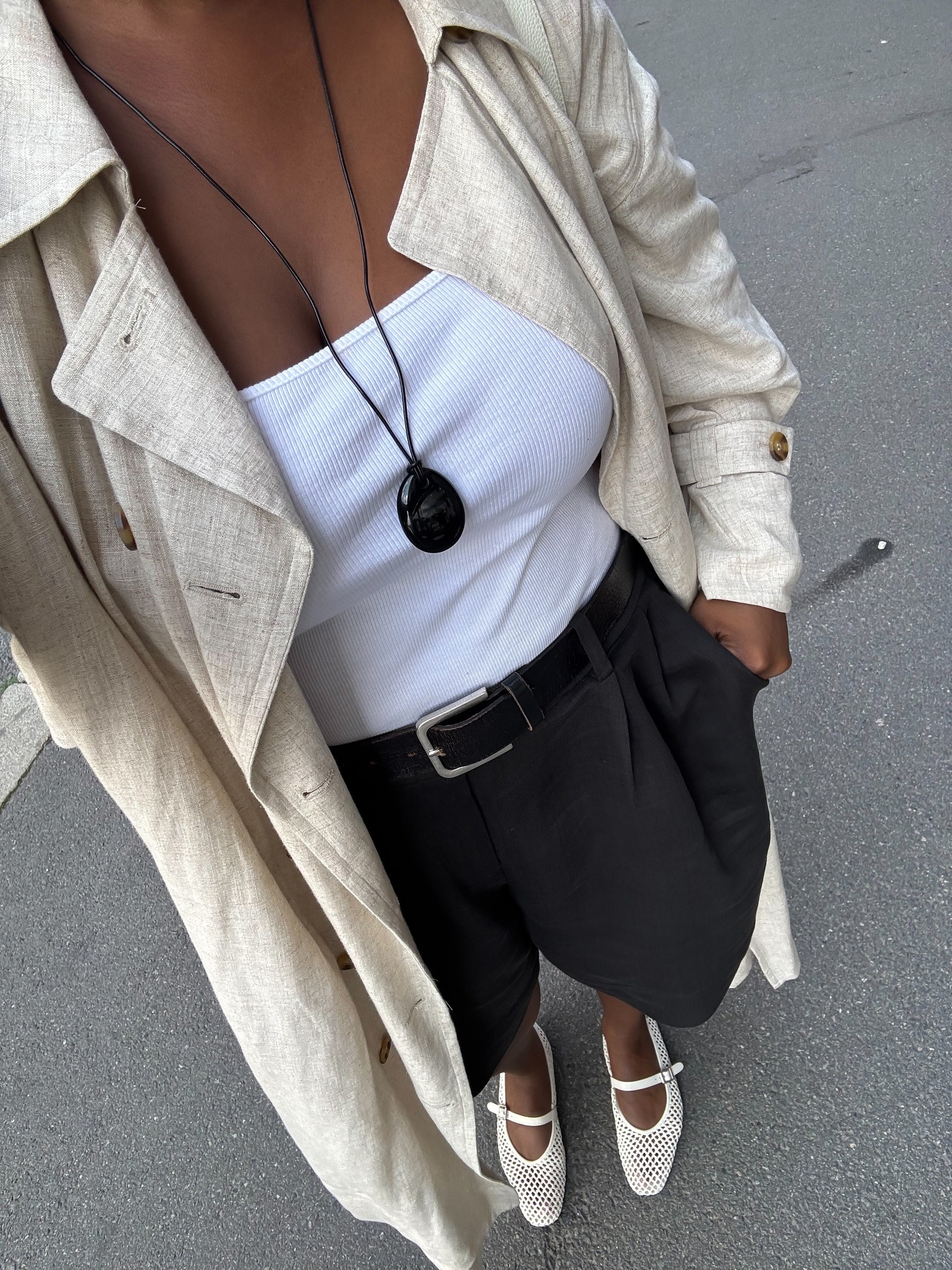 Woman in white tank top, black shorts with black pendant necklace.
