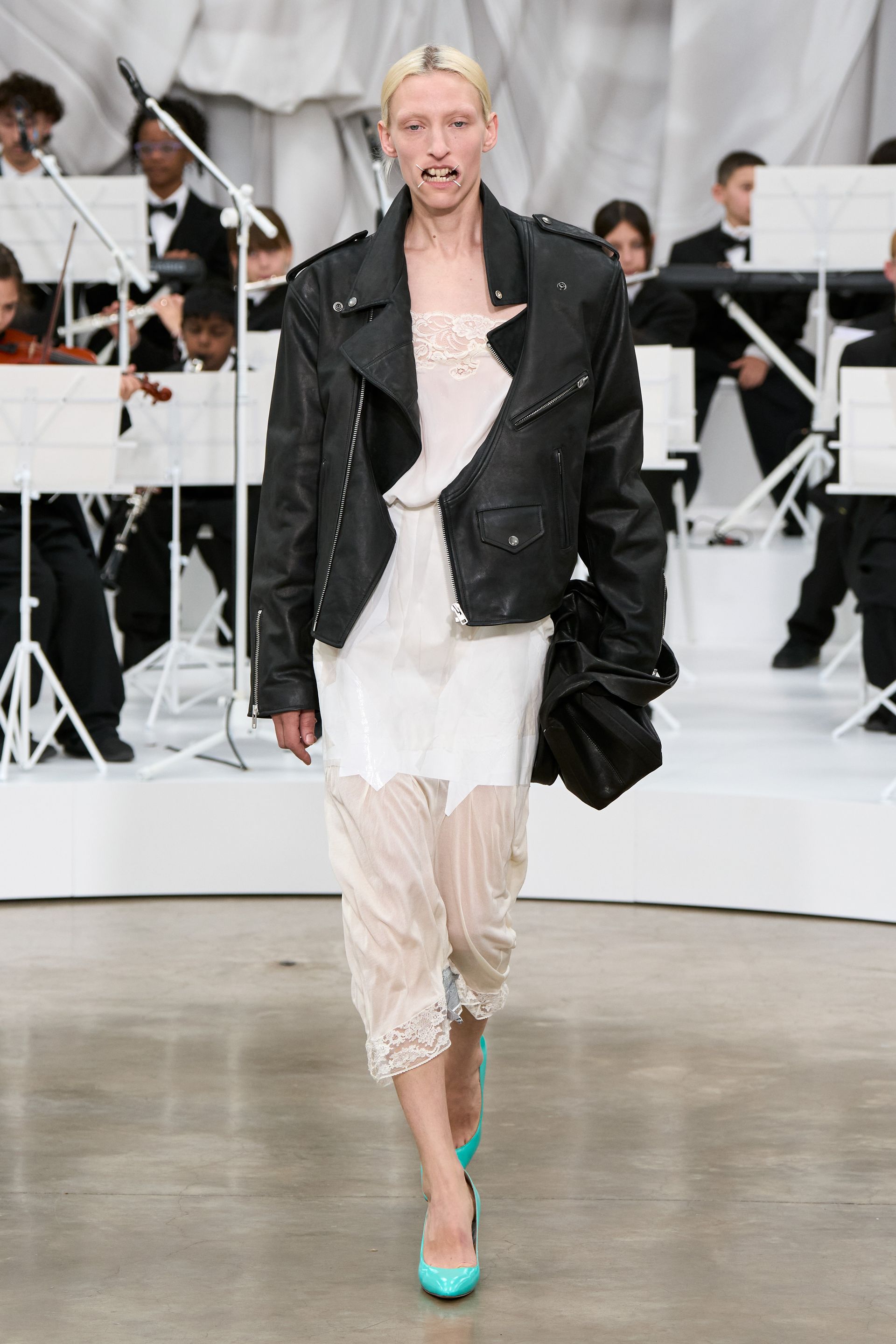 A model at the S/S 26 Maison Margiela show wearing a leather jacket with a lace slip dress and turquoise heels.