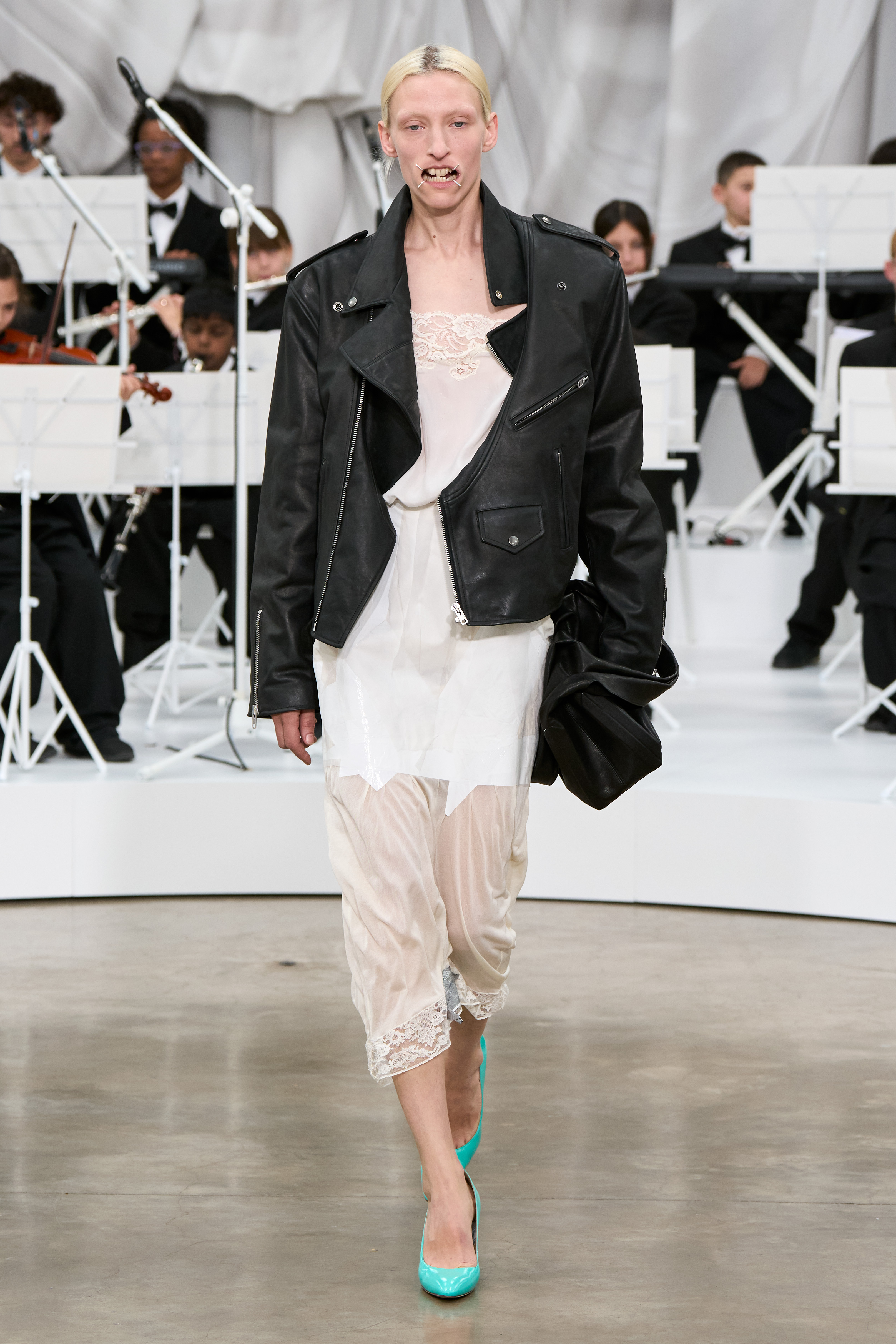 A model at the S/S 26 Maison Margiela show wearing a leather jacket with a lace slip dress and turquoise heels.