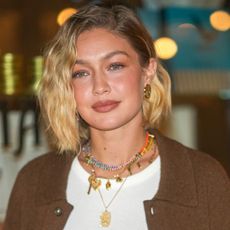 Gigi Hadid wears a white T-shirt and layered necklaces with a brown sweater