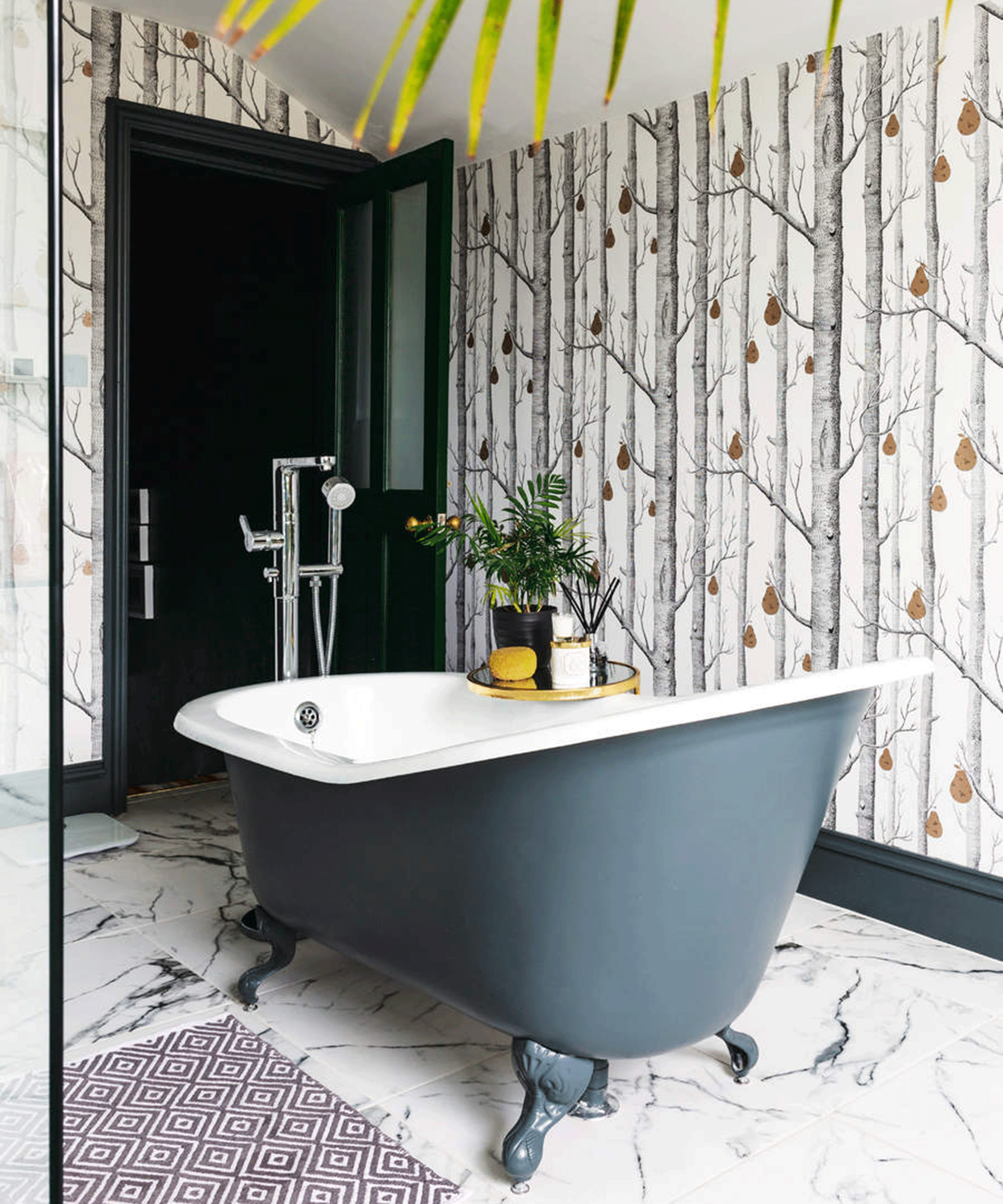 A bathroom with printed wallpaper decor, blue rolltop bath and shower head fixture