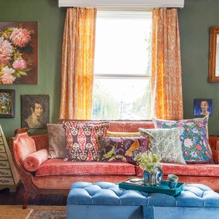 snug with dark green walls and orange sofa and pale yellow curtains framing the window
