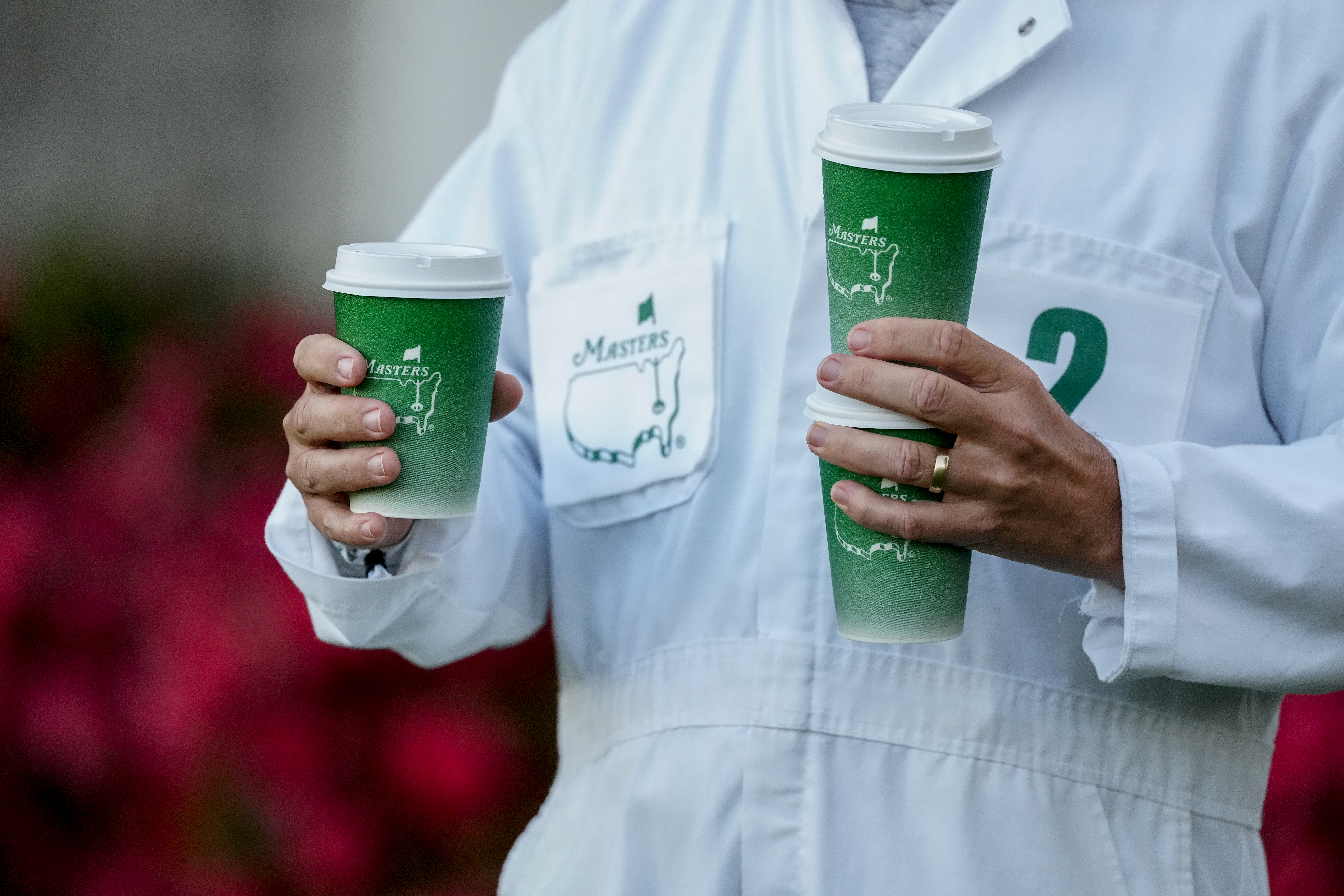 A Masters caddie holding three cups of coffee in green Masters cups