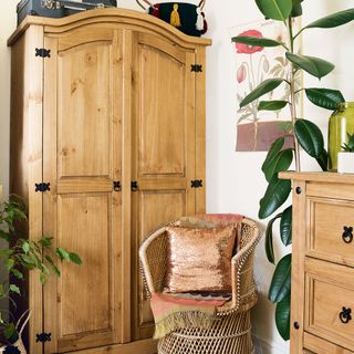 wooden wardrobe, wicker armchair, rubber plant and chest of drawers