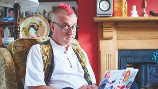 Bruce Lawson sits on an armchair with a pink mohawk and a brightly coloured waistcoat coding on his laptop.