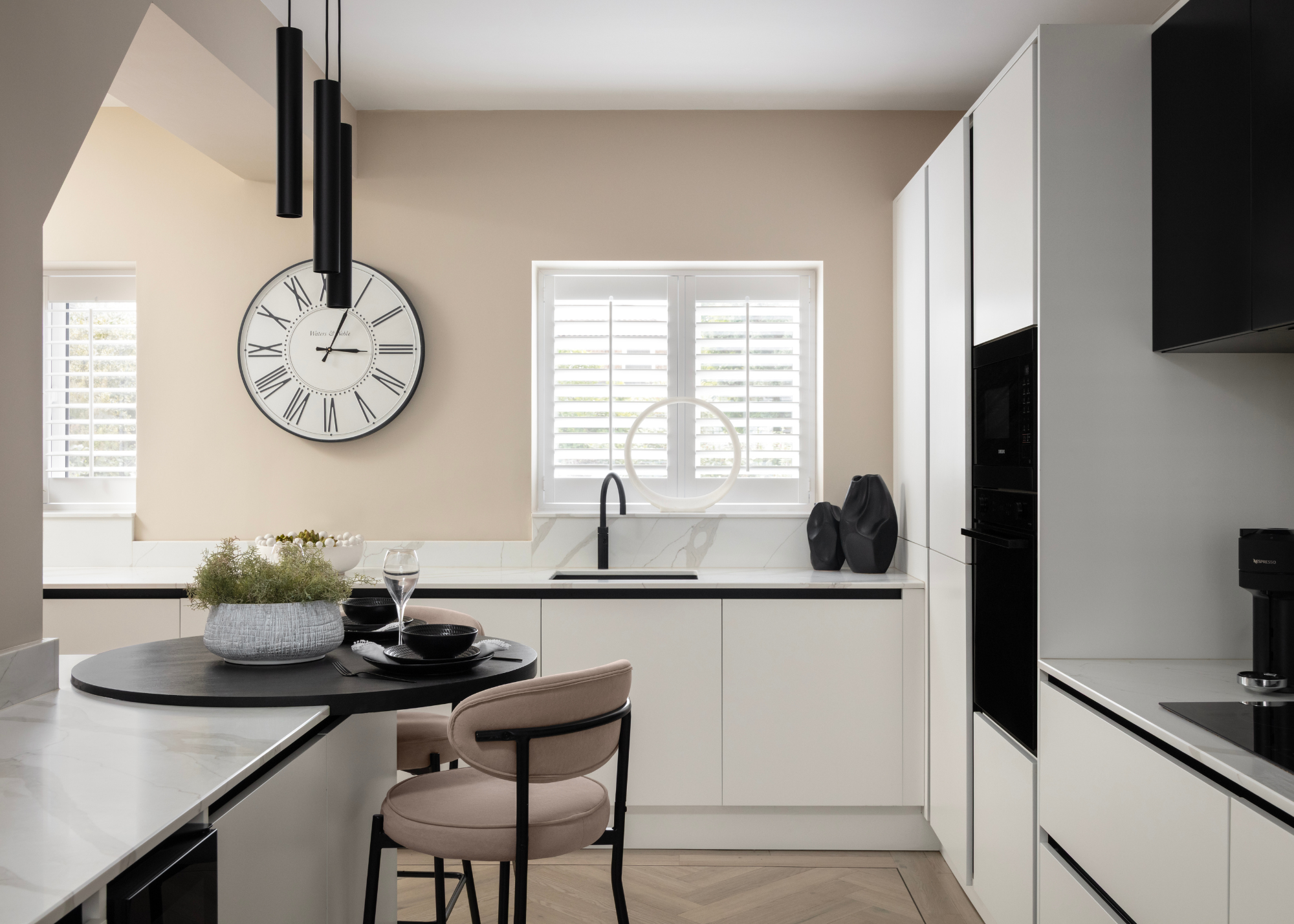 An immaculate chic modern monochrome kitchen subtly featuring a peachy pink undertone in the wall paint and bar stools at the multilevel island