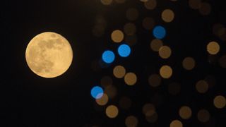 a bright full moon can be seen behind bright christmas lights