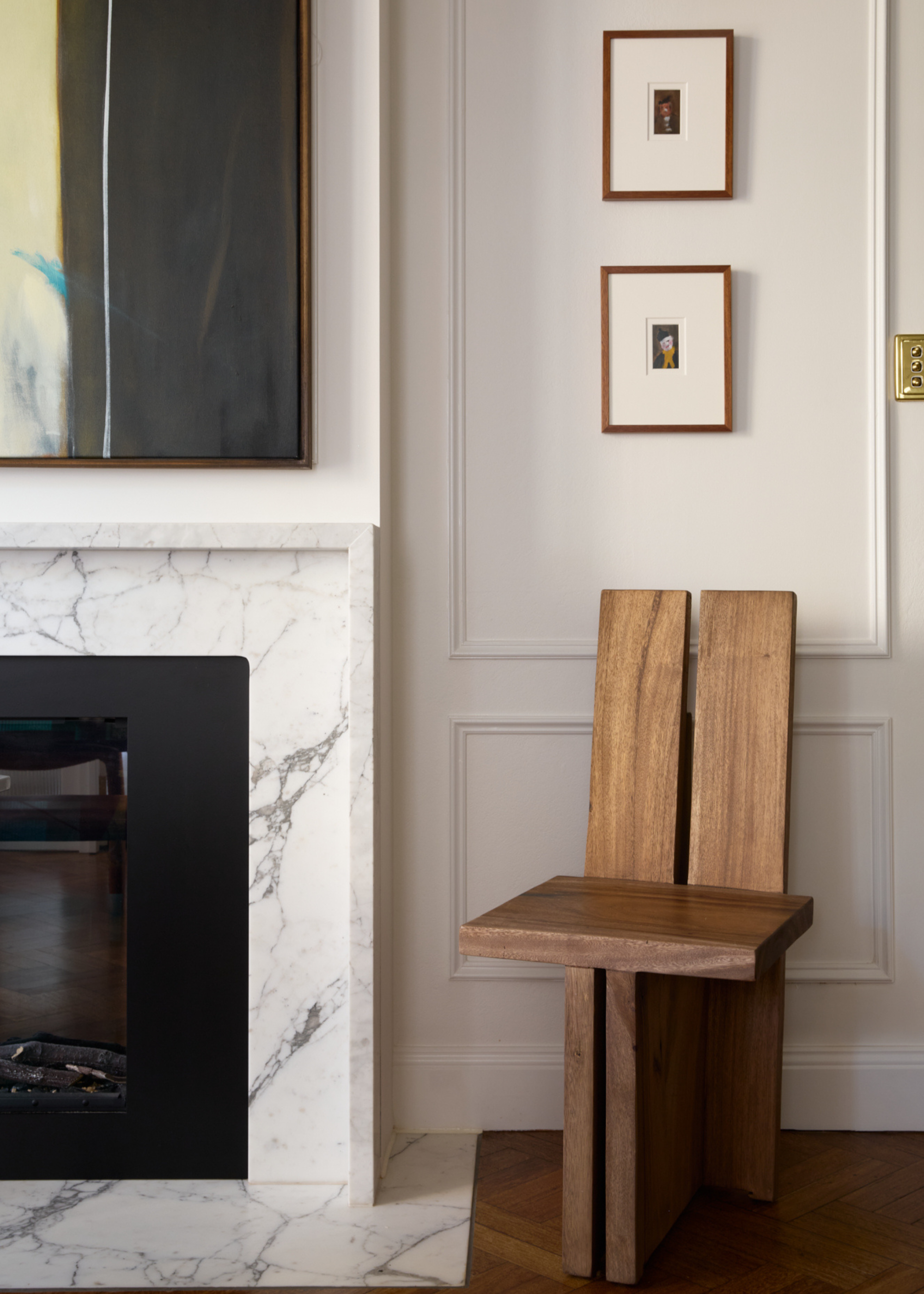 A living room with framed art, a gold switch plate, a marble fireplace, and a wooden statement chair