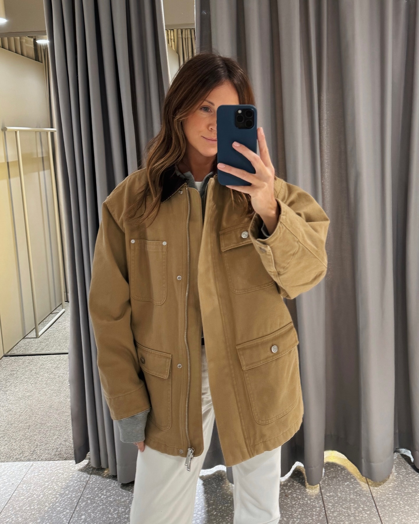 woman taking a photograph in a mirror wearing a beige canvas jacket