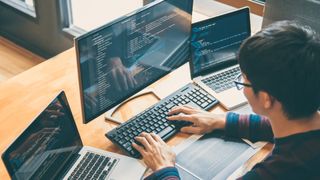 A web developer using multiple machines and displays to code