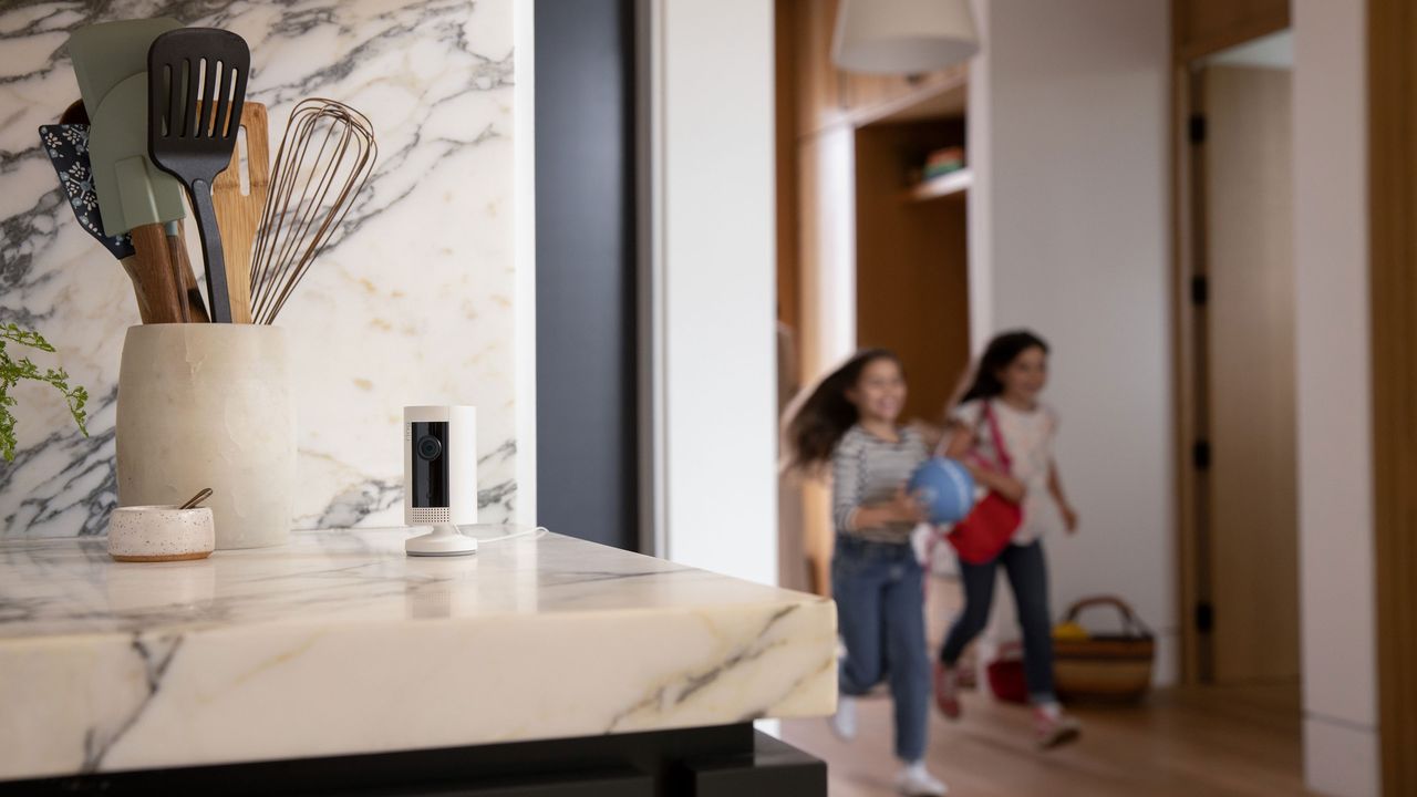 Ring indoor cam a security camera on a marble kitchen countertop with children running in the background