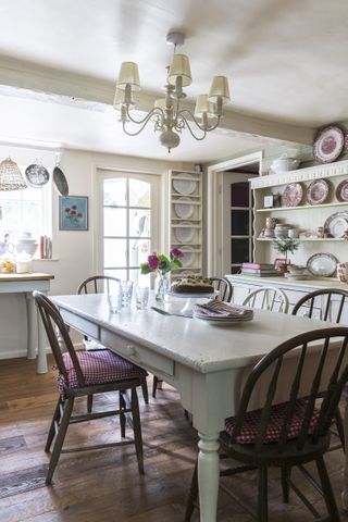 Country kitchen with wooden white dining table mauve chairs and teaware on display in open shelving
