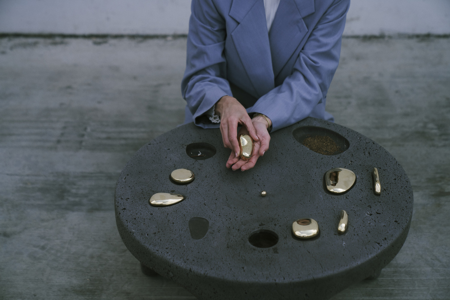 An image of a person in a blue blazer in front of a volcanic stone table with insets for metallic objects.