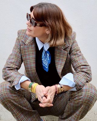 A woman wearing a tweed trouser suit with a shirt and necktie